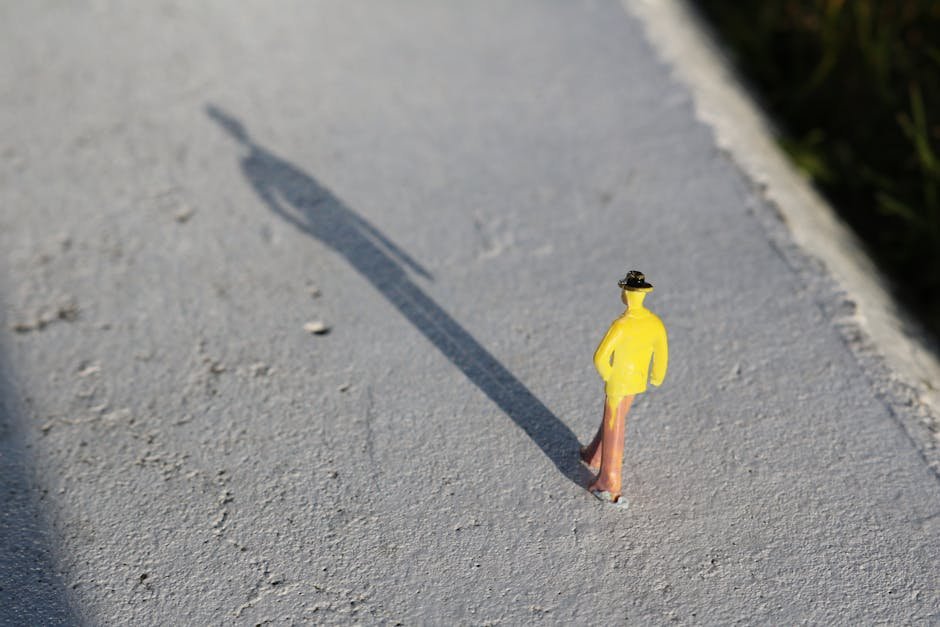 A close-up image of a toy figure in yellow clothing casting a long shadow on a concrete surface.