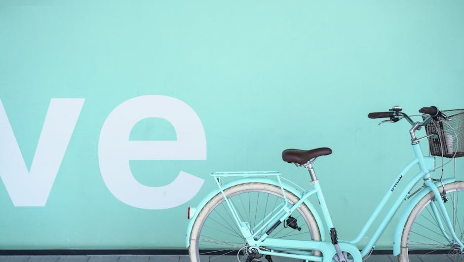 Pastel blue bicycle parked against a teal wall with partial text visible, offering modern aesthetics.